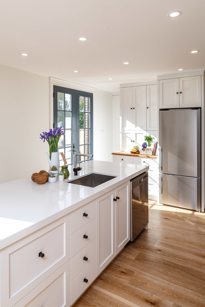 Inredning av ett skandinaviskt mellanstort kök, med vita skåp, bänkskiva i kvarts, grått stänkskydd, stänkskydd i mosaik, rostfria vitvaror, ljust trägolv och en köksö