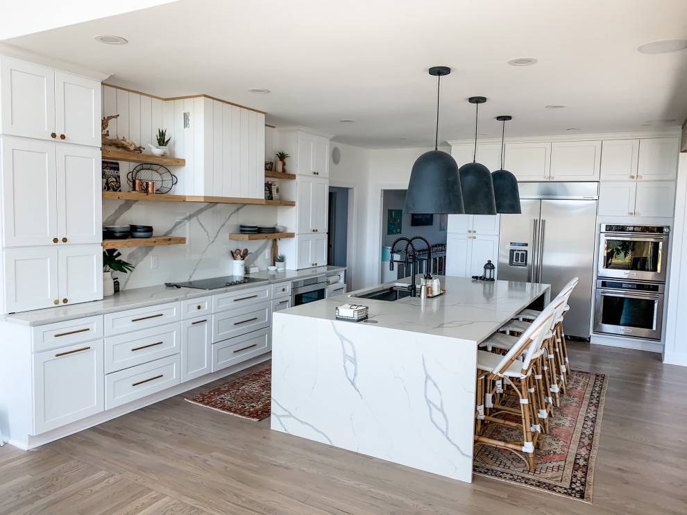 Bild på ett stort skandinaviskt vit vitt kök, med en enkel diskho, skåp i shakerstil, vita skåp, bänkskiva i kvarts, vitt stänkskydd, rostfria vitvaror, ljust trägolv, en köksö och brunt golv