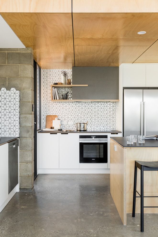 Example of a huge danish galley concrete floor and gray floor open concept kitchen design in Adelaide with flat-panel cabinets, white cabinets, solid surface countertops, white backsplash, ceramic backsplash, stainless steel appliances and an island