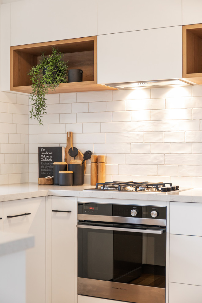アデレードにある北欧スタイルのおしゃれなコの字型キッチン (アンダーカウンターシンク、フラットパネル扉のキャビネット、白いキャビネット、クオーツストーンカウンター、白いキッチンパネル、サブウェイタイルのキッチンパネル、白い調理設備、ラミネートの床、茶色い床、白いキッチンカウンター) の写真