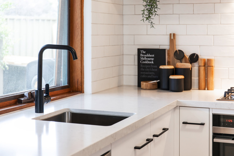 Photo of a scandi u-shaped kitchen in Adelaide with a submerged sink, flat-panel cabinets, white cabinets, engineered stone countertops, white splashback, metro tiled splashback, white appliances, laminate floors, brown floors and white worktops.
