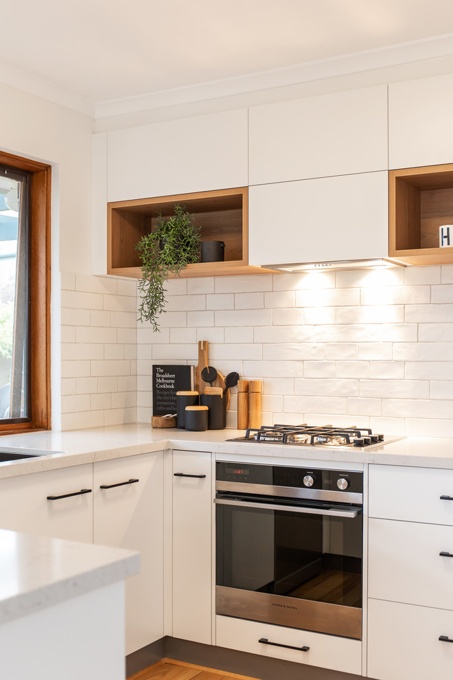 Bild på ett minimalistiskt vit vitt u-kök, med en undermonterad diskho, släta luckor, vita skåp, bänkskiva i kvarts, vitt stänkskydd, stänkskydd i tunnelbanekakel, vita vitvaror, laminatgolv och brunt golv