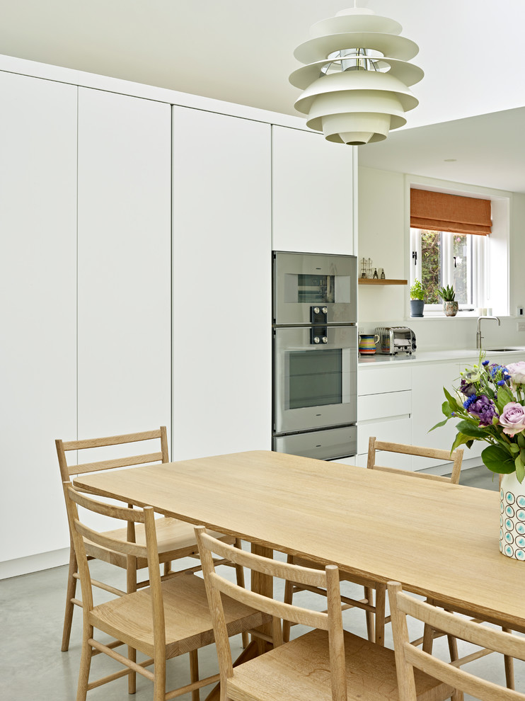 Inredning av ett minimalistiskt mellanstort vit linjärt vitt kök och matrum, med en undermonterad diskho, släta luckor, vita skåp, bänkskiva i koppar, vitt stänkskydd, rostfria vitvaror, betonggolv, en köksö och grått golv