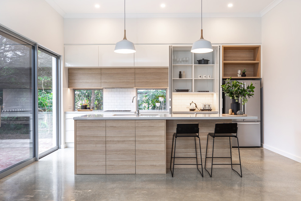 Design ideas for a medium sized contemporary galley kitchen in Adelaide with a submerged sink, flat-panel cabinets, light wood cabinets, engineered stone countertops, white splashback, metro tiled splashback, stainless steel appliances, concrete flooring, an island, grey floors and grey worktops.