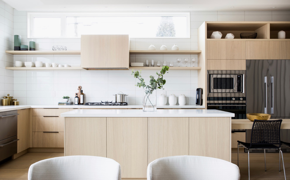 Skandinavische Wohnküche in L-Form mit flächenbündigen Schrankfronten, hellen Holzschränken, Küchenrückwand in Weiß, Küchengeräten aus Edelstahl, hellem Holzboden, Kücheninsel, beigem Boden und weißer Arbeitsplatte in Vancouver