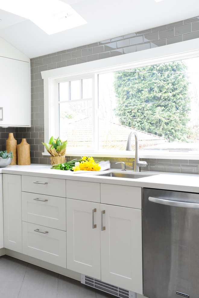 Small 1950s l-shaped porcelain tile eat-in kitchen photo in Vancouver with an undermount sink, shaker cabinets, white cabinets, solid surface countertops, gray backsplash, glass tile backsplash, stainless steel appliances and no island