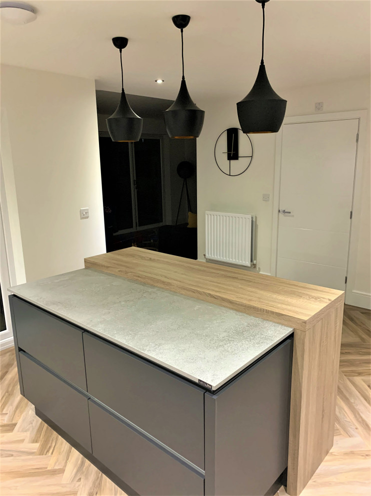 Photo of a small scandinavian l-shaped kitchen/diner in Other with a double-bowl sink, flat-panel cabinets, light wood cabinets, concrete worktops, black appliances, vinyl flooring and an island.