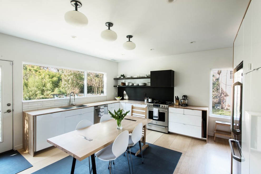 Example of a danish u-shaped light wood floor eat-in kitchen design in Richmond with an undermount sink, flat-panel cabinets, white cabinets, wood countertops and stainless steel appliances