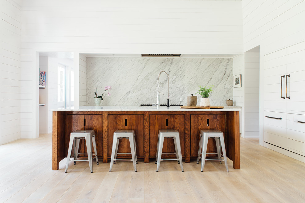 Skandinavisk inredning av ett kök, med släta luckor, skåp i mellenmörkt trä, marmorbänkskiva, vitt stänkskydd, stänkskydd i sten, integrerade vitvaror, ljust trägolv och en köksö