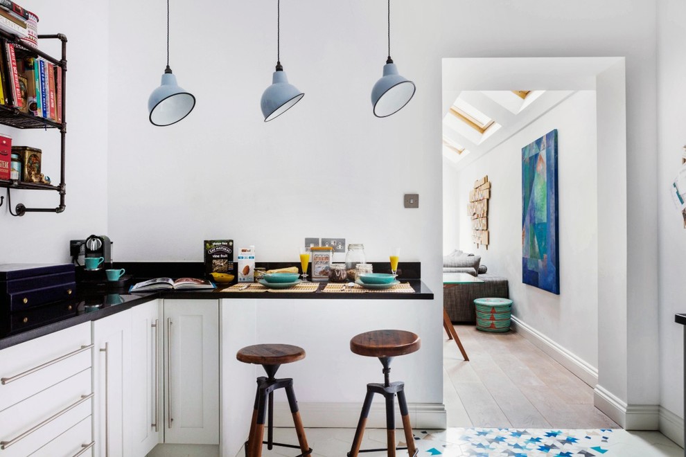 Kleine Skandinavische Küche mit flächenbündigen Schrankfronten, weißen Schränken, Granit-Arbeitsplatte, Küchengeräten aus Edelstahl und Porzellan-Bodenfliesen in London