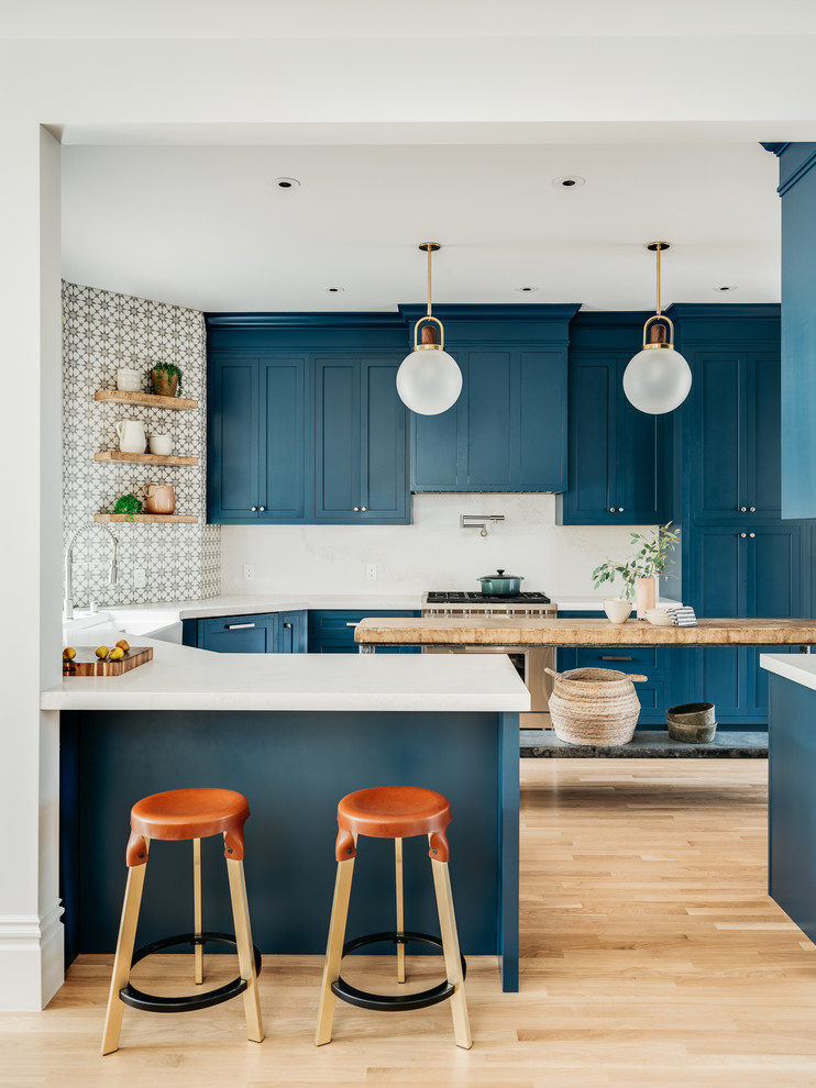 This is an example of a scandinavian u-shaped kitchen in San Francisco with shaker cabinets, blue cabinets, stainless steel appliances, light hardwood flooring, an island, white worktops and multi-coloured splashback.