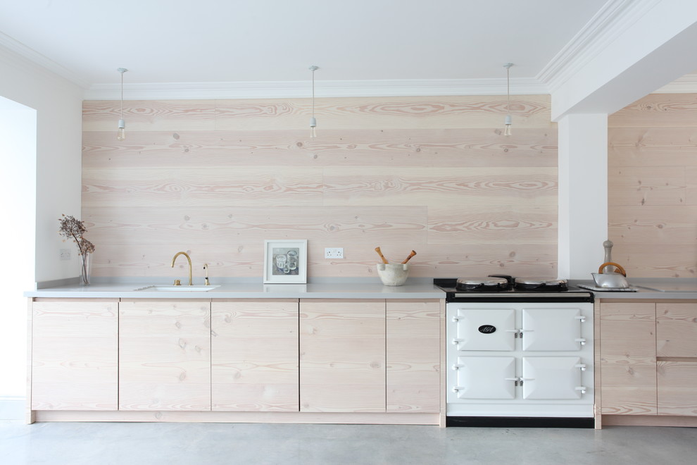 Diseño de cocina lineal nórdica con puertas de armario de madera clara, suelo de cemento, fregadero bajoencimera, armarios con paneles lisos y electrodomésticos blancos