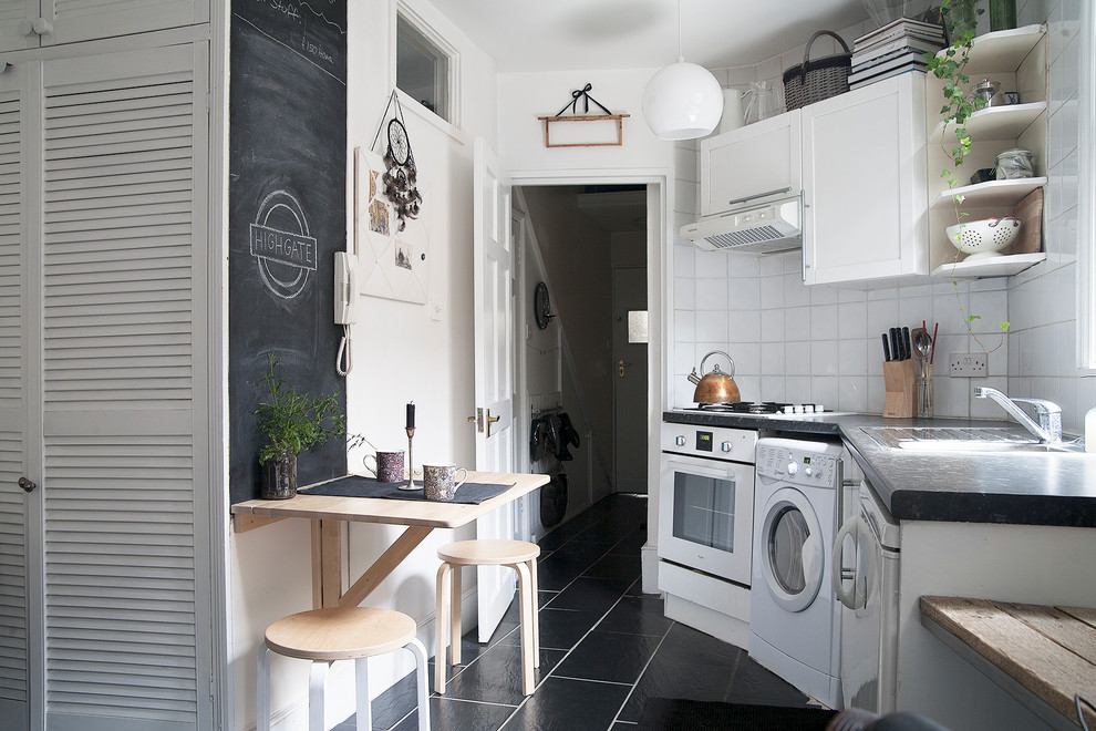 Photo of a small scandi single-wall kitchen in London with shaker cabinets, white cabinets, white splashback, ceramic splashback, white appliances and black floors.