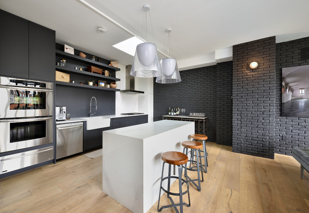 Diseño de cocina nórdica abierta con fregadero sobremueble, armarios abiertos, puertas de armario negras, salpicadero negro, electrodomésticos de acero inoxidable, suelo de madera clara y una isla