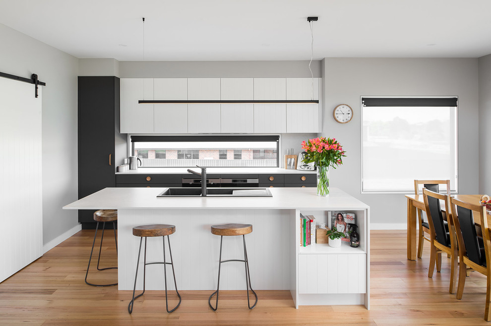 Inspiration for a scandinavian galley open plan kitchen in Hobart with a built-in sink, flat-panel cabinets, white cabinets, medium hardwood flooring, an island, brown floors and white worktops.