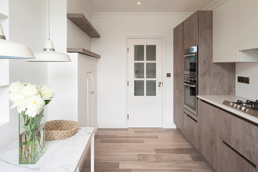 Photo of a medium sized traditional l-shaped enclosed kitchen in London with a single-bowl sink, flat-panel cabinets, composite countertops, white splashback, ceramic splashback, porcelain flooring, no island and white worktops.