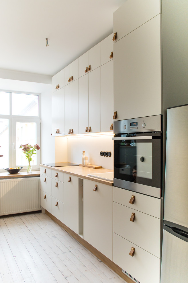 Foto di una cucina scandinava con ante lisce, ante bianche, top in legno, lavello da incasso, paraspruzzi bianco, elettrodomestici in acciaio inossidabile, parquet chiaro e pavimento beige