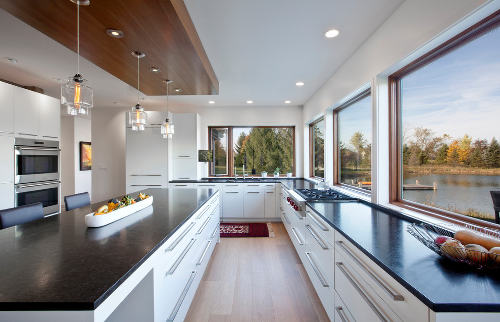 Inspiration for a mid-sized contemporary l-shaped light wood floor eat-in kitchen remodel with an undermount sink, flat-panel cabinets, white cabinets, granite countertops, paneled appliances and an island