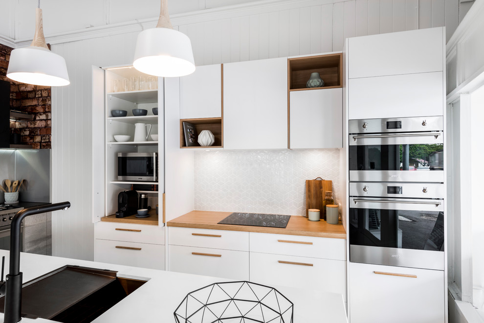 Photo of a scandi galley kitchen in Brisbane with a submerged sink, flat-panel cabinets, white cabinets, engineered stone countertops, white splashback, ceramic splashback, stainless steel appliances, ceramic flooring and an island.