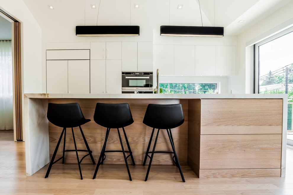 This is an example of a medium sized scandi galley kitchen/diner in Montreal with flat-panel cabinets, white cabinets, light hardwood flooring and an island.