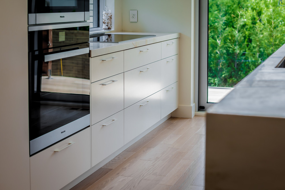 Diseño de cocina comedor nórdica de tamaño medio con armarios con paneles lisos, puertas de armario blancas, suelo de madera clara y una isla