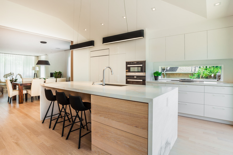 Photo of a medium sized scandi galley kitchen/diner in Montreal with flat-panel cabinets, white cabinets, light hardwood flooring and an island.
