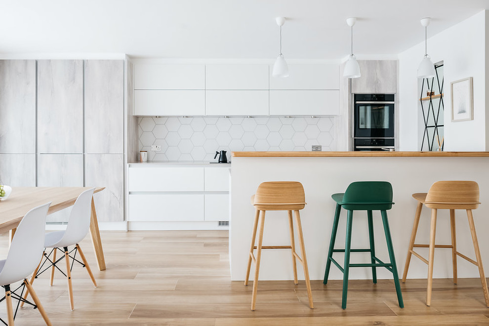 Inspiration for a large scandinavian galley kitchen/diner in Cambridgeshire with flat-panel cabinets, white splashback, ceramic splashback, integrated appliances, ceramic flooring, a breakfast bar, brown floors, white cabinets, wood worktops and beige worktops.