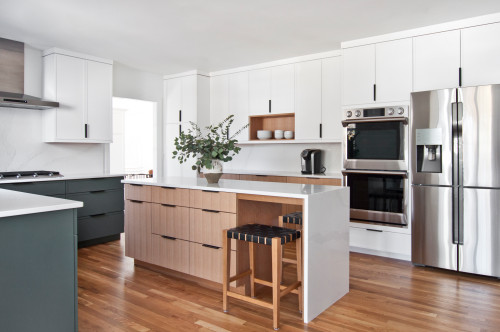 Premium RTA cabinets Canada: Minimalist Scandinavian kitchen with white & moss green flat cabinets, waterfall stone-topped wood island, black handles, built-in double oven and stainless steel refrigerator.