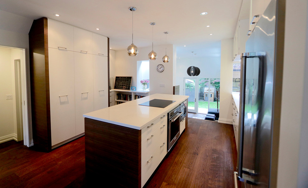 Example of a mid-sized minimalist galley medium tone wood floor and brown floor open concept kitchen design in Toronto with flat-panel cabinets, white cabinets, stainless steel appliances, an island and an undermount sink