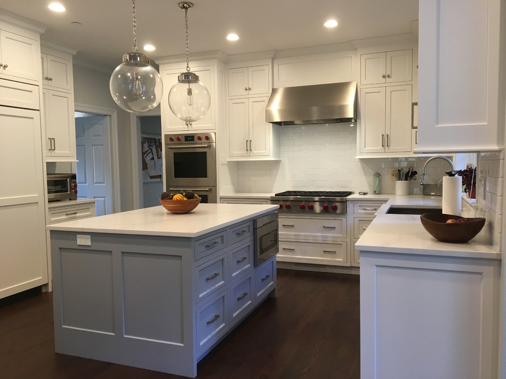 Inspiration for a mid-sized transitional u-shaped dark wood floor and brown floor eat-in kitchen remodel in New York with a double-bowl sink, raised-panel cabinets, white cabinets, solid surface countertops, white backsplash, subway tile backsplash, stainless steel appliances and an island