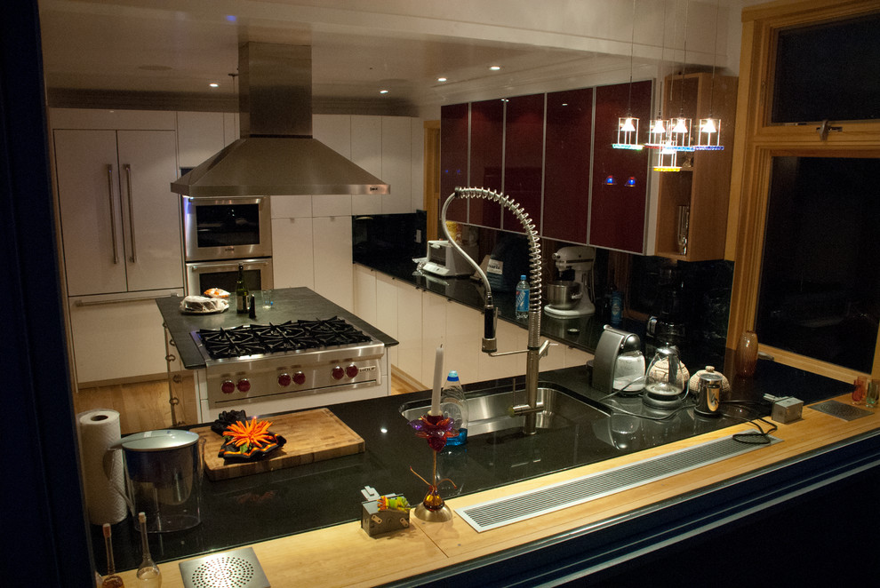 Modern inredning av ett mellanstort kök, med en undermonterad diskho, luckor med glaspanel, vita skåp, marmorbänkskiva, rött stänkskydd, stänkskydd i sten, rostfria vitvaror, ljust trägolv och en köksö