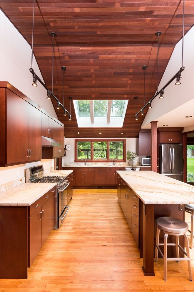 Inredning av ett modernt stort u-kök, med släta luckor, skåp i mellenmörkt trä, rostfria vitvaror, mellanmörkt trägolv, en köksö, brunt golv, en undermonterad diskho och granitbänkskiva