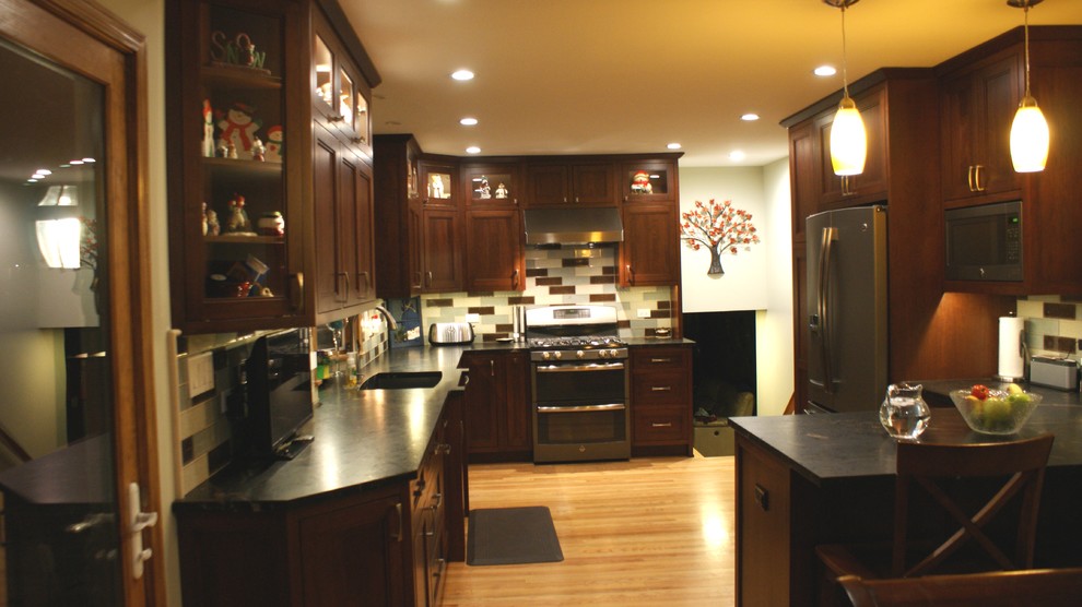 Example of a mid-sized classic u-shaped light wood floor enclosed kitchen design in Chicago with an undermount sink, shaker cabinets, medium tone wood cabinets, granite countertops, multicolored backsplash, subway tile backsplash, stainless steel appliances and a peninsula