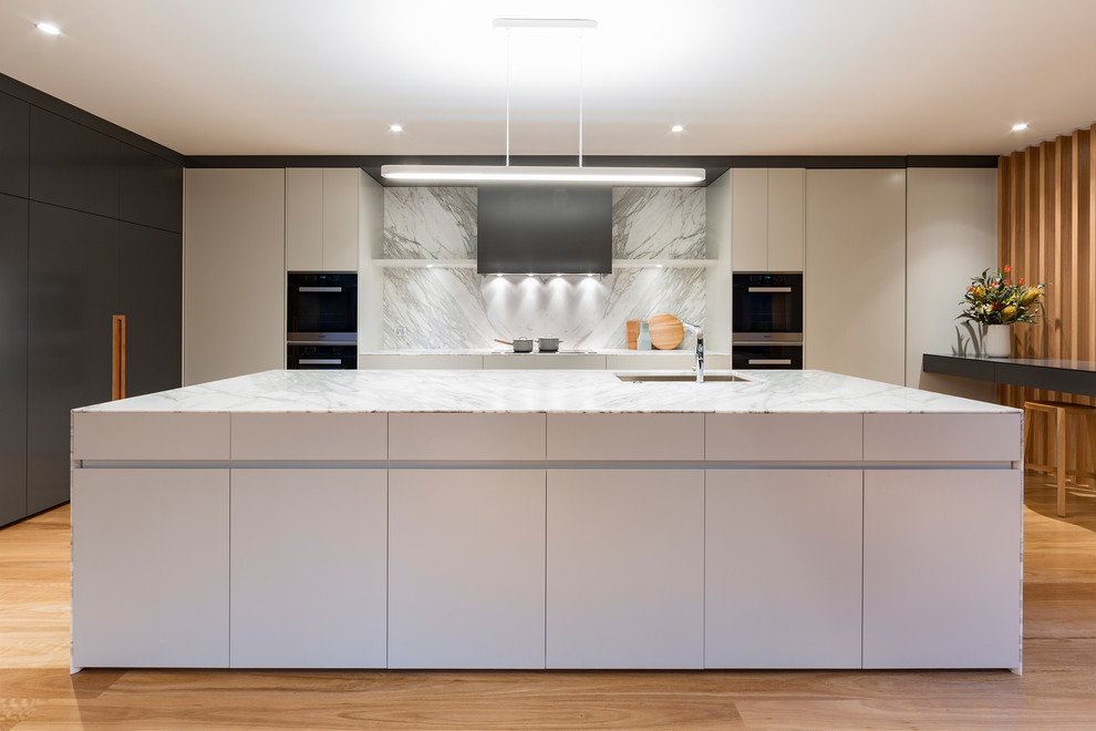 Foto di una grande cucina design con lavello sottopiano, top in marmo, paraspruzzi bianco, elettrodomestici in acciaio inossidabile e parquet chiaro