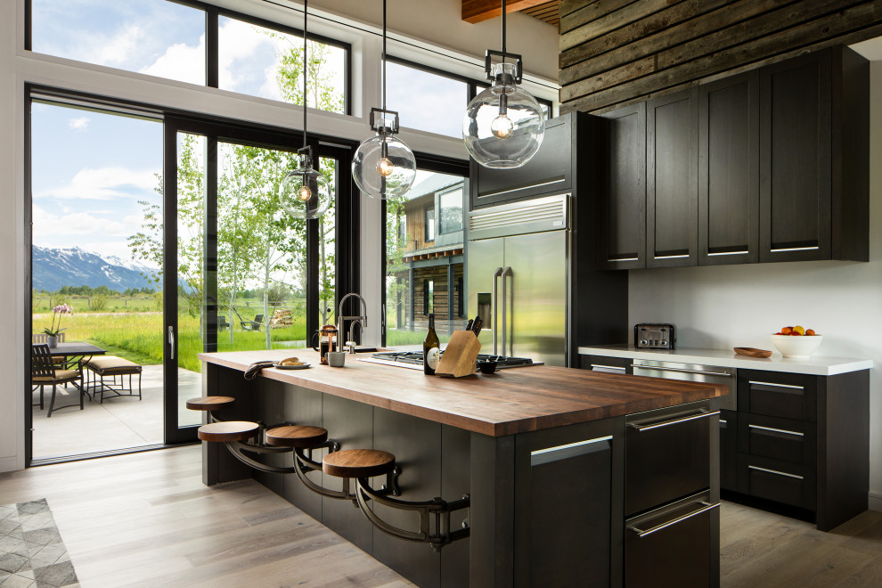 Cette image montre une cuisine parallèle design en bois foncé avec un placard à porte shaker, un électroménager en acier inoxydable, un sol en bois brun, îlot, un sol marron et un plan de travail blanc.