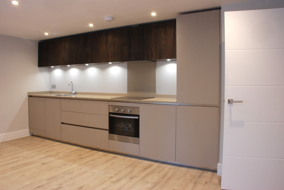 Photo of a medium sized contemporary single-wall open plan kitchen in Surrey with a single-bowl sink, flat-panel cabinets, beige cabinets, composite countertops, white splashback, glass sheet splashback, black appliances, light hardwood flooring, no island and beige floors.