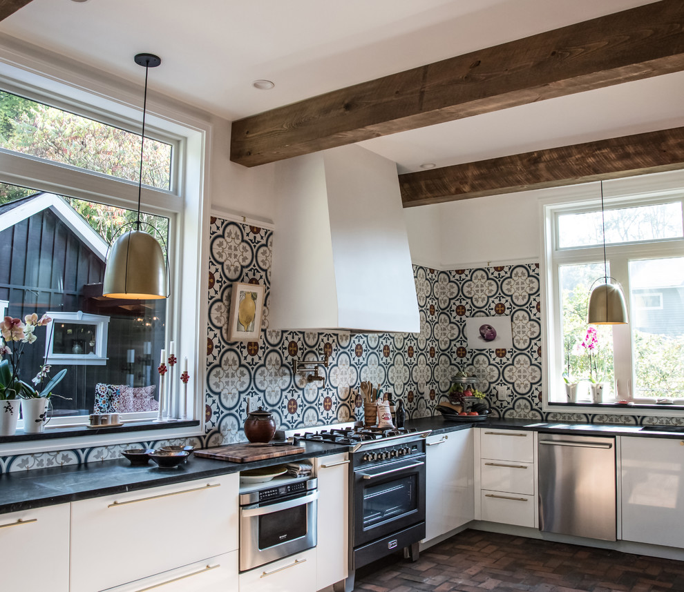 This is an example of a medium sized farmhouse u-shaped kitchen/diner with a submerged sink, flat-panel cabinets, white cabinets, soapstone worktops, multi-coloured splashback, cement tile splashback, stainless steel appliances, brick flooring, no island and red floors.