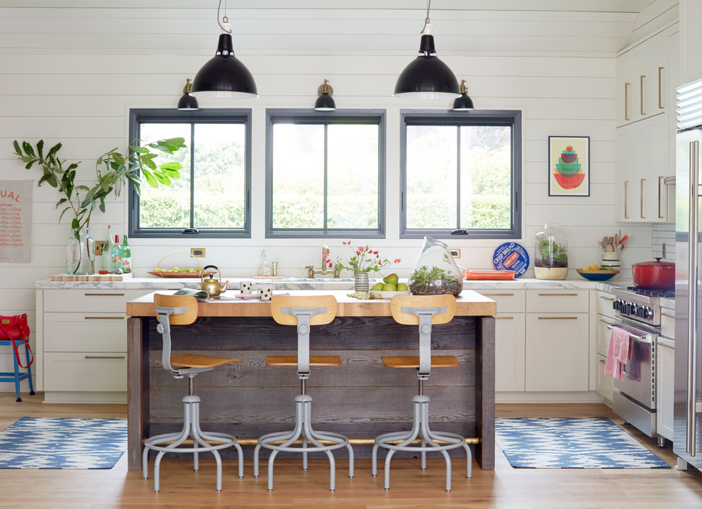 Foto på ett lantligt l-kök, med skåp i shakerstil, vita skåp, rostfria vitvaror, ljust trägolv och en köksö