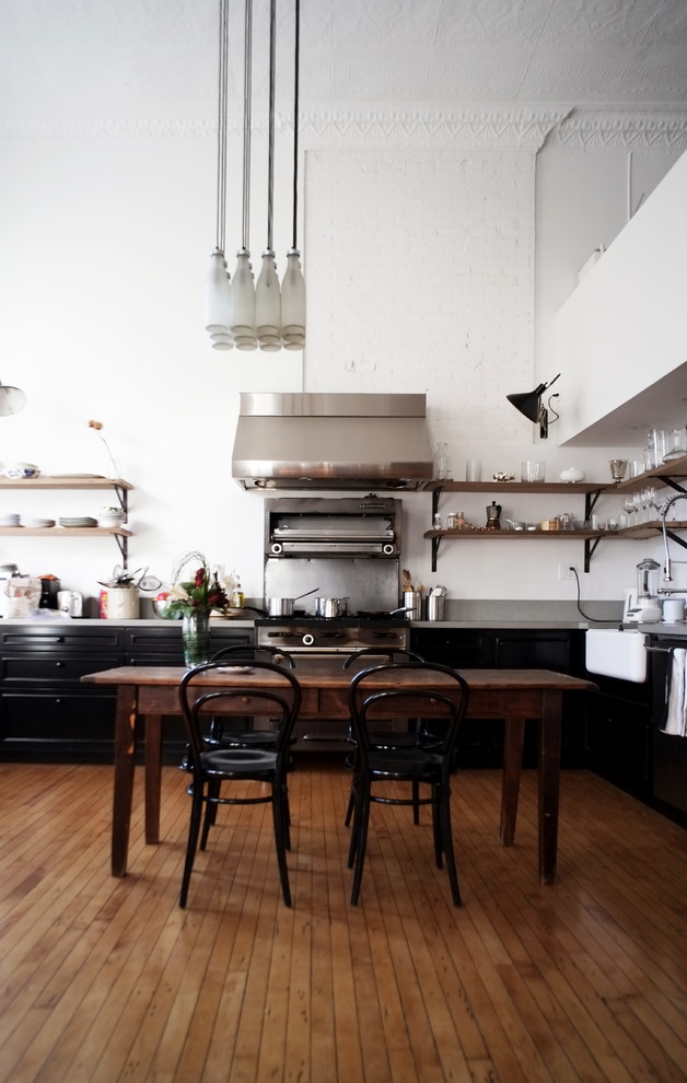 This is an example of an industrial kitchen/diner in New York with a belfast sink, open cabinets, stainless steel appliances and medium hardwood flooring.