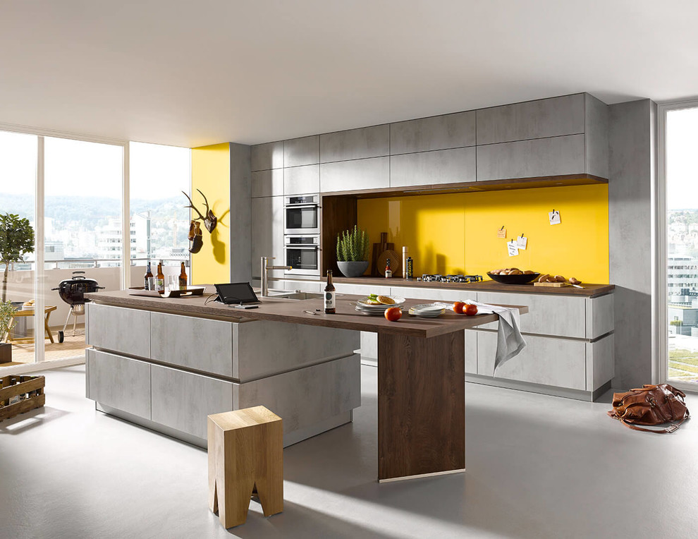 Inspiration for a large modern single-wall open plan kitchen in Surrey with a submerged sink, flat-panel cabinets, grey cabinets, wood worktops, yellow splashback, stainless steel appliances, concrete flooring, an island and grey floors.