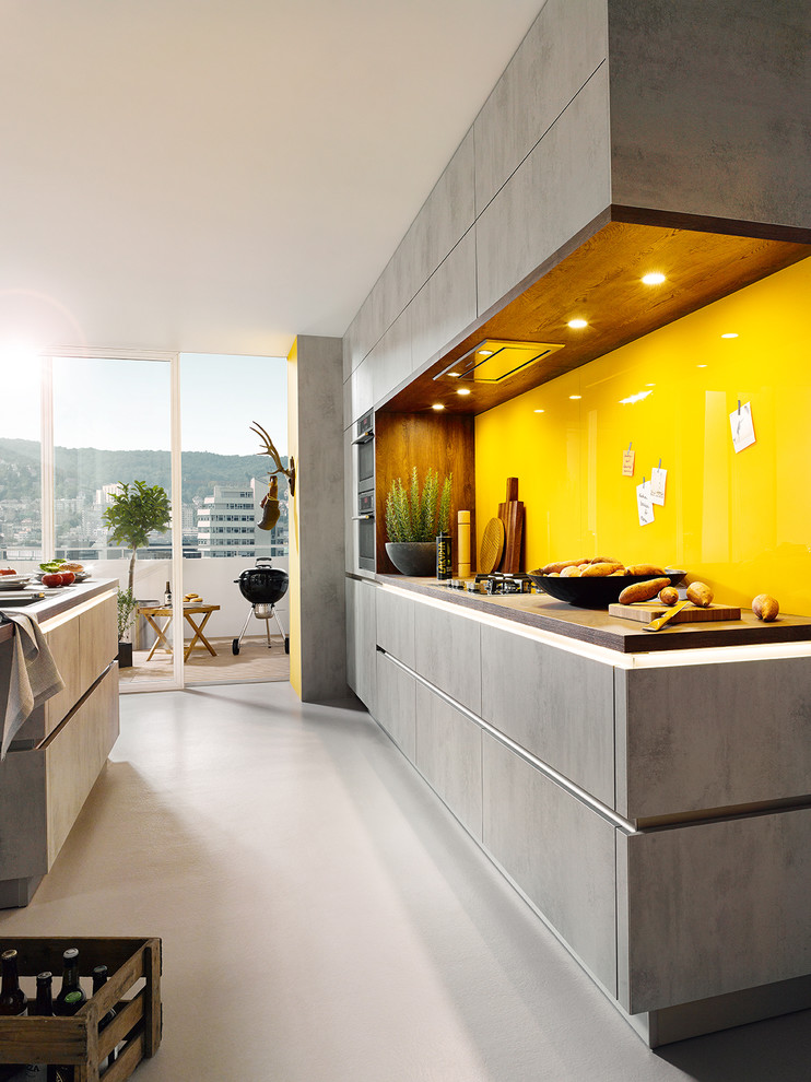 Design ideas for a medium sized modern galley kitchen in Surrey with a submerged sink, flat-panel cabinets, grey cabinets, wood worktops, yellow splashback, glass sheet splashback, stainless steel appliances, cement flooring and an island.