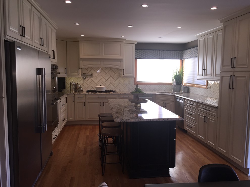 This is an example of a large classic u-shaped open plan kitchen in Chicago with raised-panel cabinets, white cabinets, granite worktops, white splashback, ceramic splashback, stainless steel appliances, light hardwood flooring and an island.