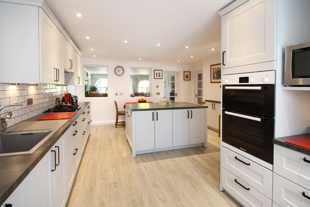 Large classic galley kitchen pantry in Sussex with a single-bowl sink, recessed-panel cabinets, grey cabinets, laminate countertops, white splashback, ceramic splashback, integrated appliances, vinyl flooring and an island.