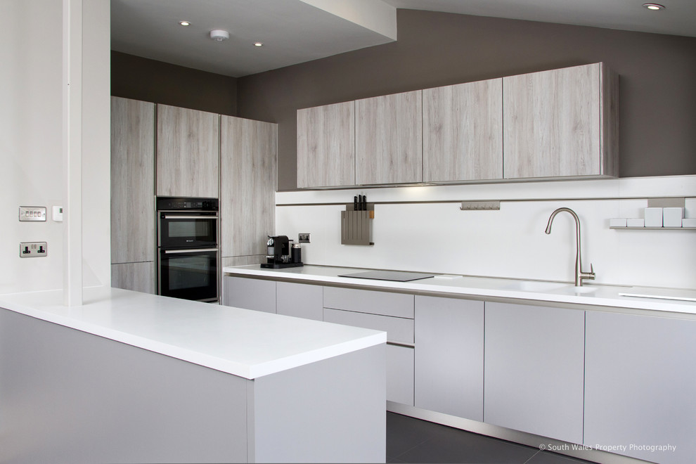 Design ideas for a medium sized contemporary galley kitchen/diner in Other with an integrated sink, flat-panel cabinets, light wood cabinets, white splashback, black appliances and ceramic flooring.