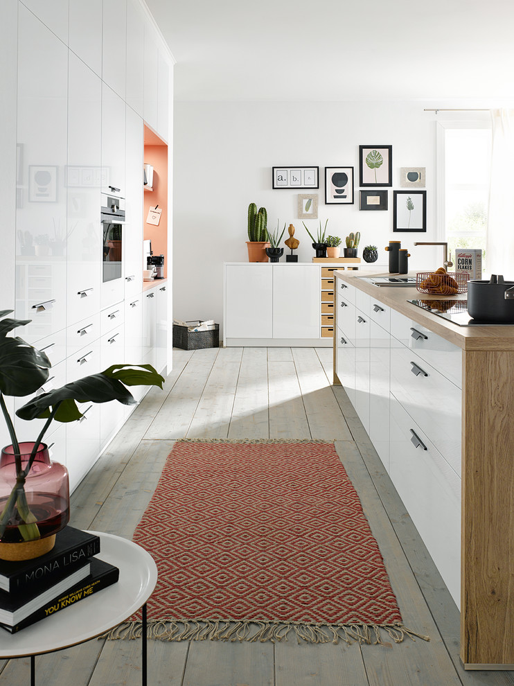 Offene, Zweizeilige Moderne Küche mit flächenbündigen Schrankfronten, weißen Schränken, Arbeitsplatte aus Holz, Elektrogeräten mit Frontblende, hellem Holzboden, Kücheninsel und grauem Boden in Sonstige
