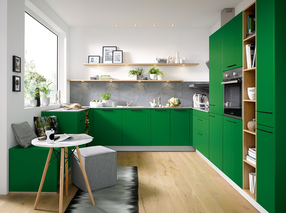 Trendy u-shaped light wood floor and beige floor kitchen photo in Other with flat-panel cabinets, green cabinets, gray backsplash and paneled appliances