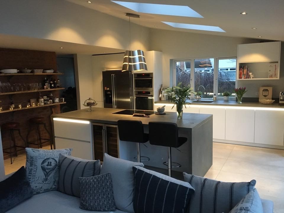 Large contemporary open plan kitchen in Cardiff with flat-panel cabinets, white cabinets, an island, concrete worktops, stainless steel appliances and ceramic flooring.