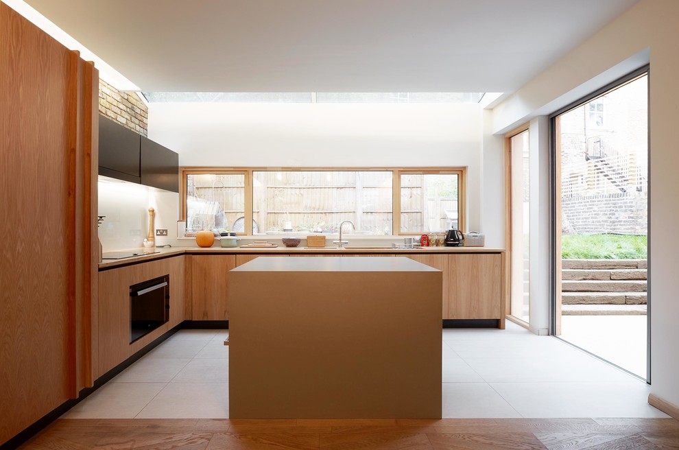 Modern inredning av ett mellanstort kök, med släta luckor, skåp i ljust trä, vitt stänkskydd, integrerade vitvaror, klinkergolv i porslin och en köksö