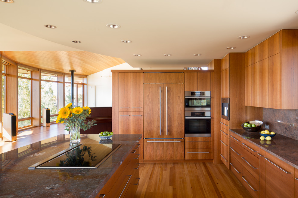 Foto på ett mellanstort funkis kök, med släta luckor, skåp i mellenmörkt trä, granitbänkskiva, grönt stänkskydd, stänkskydd i sten, mellanmörkt trägolv och en köksö