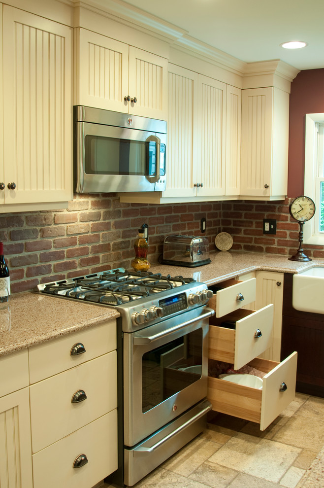 Klassisk inredning av ett litet kök, med en rustik diskho, skåp i shakerstil, bänkskiva i kvarts, rött stänkskydd, rostfria vitvaror, travertin golv och en köksö